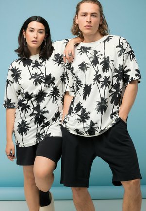 Dos modelos posan frente a un fondo azul, vestidos con camisas blancas a juego estampadas con palmeras y pantalones cortos negros.
