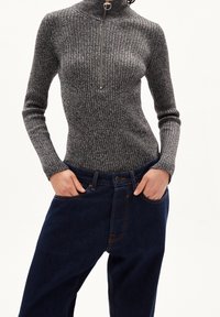 Suéter de cuello alto acanalado en gris oscuro con un medio cierre en la parte delantera, combinado con jeans de mezclilla azul oscuro que tienen bolsillos y costuras de contraste.