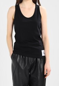 Débardeur noir sans manches en tissu coton doux, avec un col rond et une petite étiquette logo à l'ourlet. Assorti à un pantalon en cuir noir.