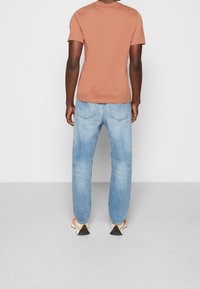 Brun formsydd t-shirt, ljusblå urtvättade jeans och mångfärgade skor med en triangulär detalj på baksidan. Enkel design, avslappnad passform.