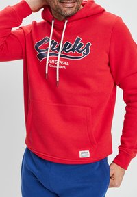 Czerwona bluza z kapturem z przednią kieszenią, granatowy nadruk "Creeks Original Since 1974" na klatce piersiowej oraz białe sznurki. Miękki materiał.