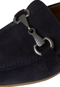 Navyblauwe suède instappers met een getextureerde zilveren accentstrik en ronde hardware. Voorzien van contrasterende blauwe stiksels langs de randen.