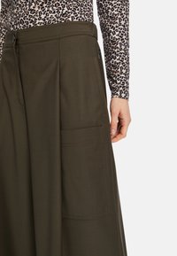 Brown wide-leg trousers in textured fabric with a side pocket and a zip closure. Styled with a patterned long-sleeve top.