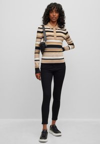 Gestreepte lange mouwen polo in beige, zwart en wit met een kraag, knopen, gecombineerd met zwarte skinny jeans en zwarte sneakers.