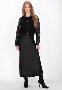Fekete kardigán flitteres ujjakkal, rövidített fazonú, elülső gombokkal, egy lebegő fekete selyemszoknyával és magas fekete magassarkú cipőkkel párosítva.