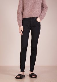 Svarta skinny jeans med en slät yta, kombinerat med en ljusrosa fluffig tröja. Bärs med svarta pälsiga klibbensandaler.