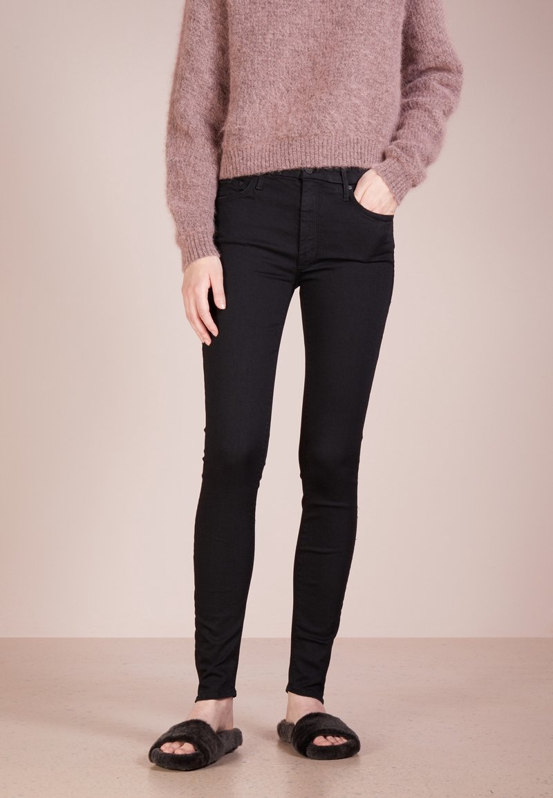 Svarta skinny jeans med en slät yta, kombinerat med en ljusrosa fluffig tröja. Bärs med svarta pälsiga klibbensandaler.