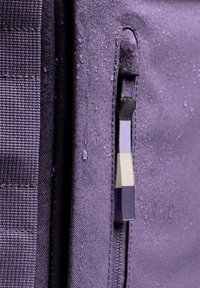 Tissu violet avec une finition texturée, comportant une poche zippée avec un tirette multicolore et des gouttes d'eau sur sa surface.