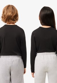 Maglietta nera a maniche lunghe con collo rotondo, abbinata a pantaloni sportivi grigi chiari. La maglietta si adatta perfettamente alla vita. Entrambi gli articoli sono senza decorazioni.