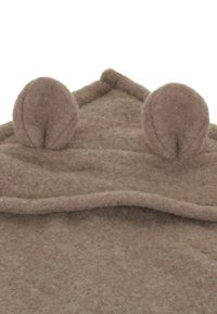 Brun, filtet stof med en blød tekstur. Har to afrundede øre-lignende detaljer på toppen. Enkel design med en foldet kantdetalje.