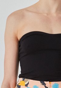 Top negro sin mangas con una textura suave, diseño ajustado y un escote limpio y redondeado. Combinado con una falda de patrón floral.