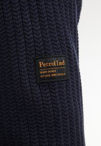Marine gebreide trui met een gestructureerd herringbonepatroon. Bevat een zwart label met gouden tekst die "Petrol Ind, Denim Driven" leest.
