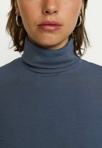 Maglione a collo alto a coste in blu scuro, caratterizzato da un design aderente e una texture morbida, con pieghe sottili all'collo.