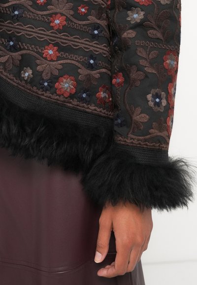 Črna vezenina jakna z cvetličnimi vzorci v rdeči in modri barvi, z teksturiranimi črnimi krznimi robovi na manšetah.