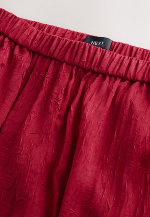 Red crinkled fabric skirt with elastic waistband. Label reads "NEXT." Smooth texture with subtle variations in surface.