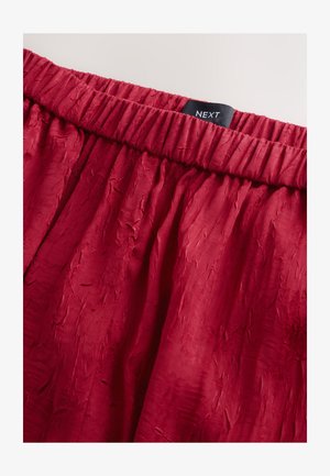 Red crinkled fabric skirt with elastic waistband. Label reads "NEXT." Smooth texture with subtle variations in surface.