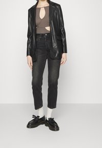 Blazer de cuero negro sobre un bodysuit marrón con recortes, combinado con jeans oscuros y zapatos de cordones negros. Medias blancas visibles.