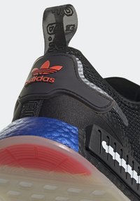 Svart atletisk sko med en texturerad stickad ovandel, röd logotyp och en flerfärgad sula med blå och rosa accenter. Mjuk gummisula.