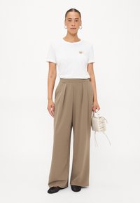 Witte T-shirt met korte mouwen en een klein, textuurhartontwerp; hoge beige wijde broek; kleine crèmekleurige handtas; zwarte platte schoenen.