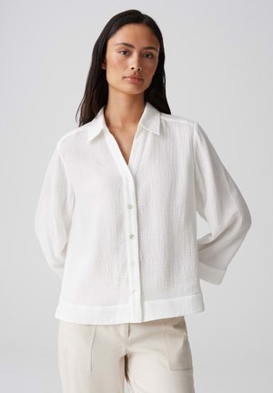 Camicia bianca con bottoni realizzata in tessuto testurizzato, dotata di colletto e maniche lunghe, con chiusura a bottoni e vestibilità rilassata.