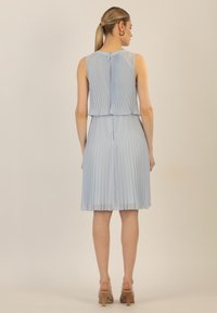 Robe plissée bleu clair avec une superposition transparente, sans manches, et un ourlet droit. Elle dispose d'une fermeture éclair au dos.