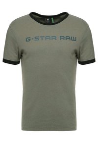 Oliivinvihreä puuvillainen t-paita, jossa on musta resori kauluksessa ja hihoissa. T-paidassa on erottuva tummansininen "G-STAR RAW" -logo. Pehmeä tekstuuri, lyhyet hihat.