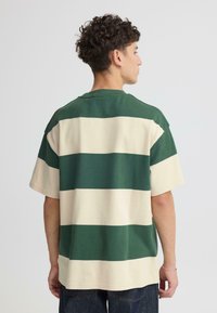 T-shirt manches courtes rayé vert et crème en coton. Présente de larges rayures horizontales et un col rond. Coupe décontractée avec une forme ample.