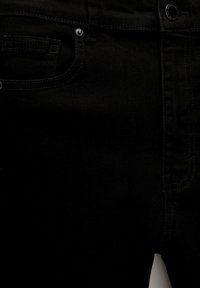 Jean en denim noir avec un design classique à cinq poches, une couture robuste et une fermeture à bouton métallique avec une texture lisse.