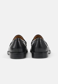 Paire de mocassins formels noirs en cuir pour hommes, vus de dos sur un fond clair uni.