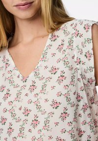 Camicia floreale bianca con scollatura a V, maniche corte e un delicato motivo di fiori rosa con dettagli verdi. Tessuto leggero.