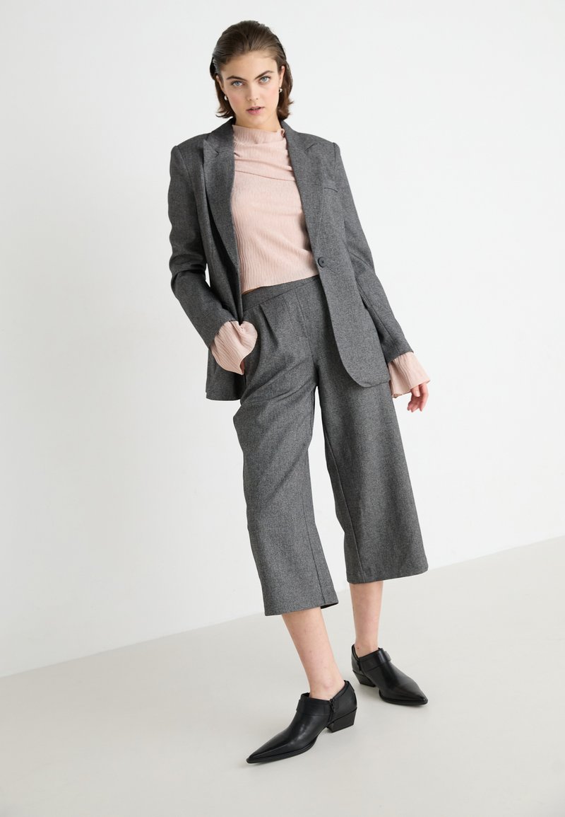 Blazer gris ajustado sobre una camiseta de canalé rosa claro, combinado con pantalones de pierna ancha grises y botines negros de punta.