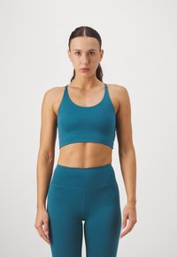 Tirkizni fitness bralette s širokom trakom, tankim naramenicama i glatkom teksturom. Uparen s visokim tirkiznim tajicama koje imaju elegantan dizajn.