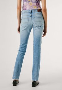 Gai zils džinsu bikses ar taisnu piegriezumu, ar divām aizmugurējām kabatām, vieglu izbalējumu un brūnu ādas uzšuvumu pie jostasvietas.