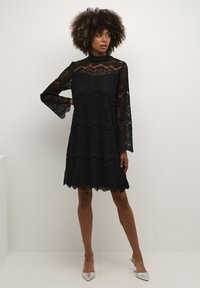 Black lace dress with long flared sleeves, scalloped hem, and intricate patterns. Paired with silver pointed-toe heels.