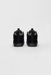 Pár černých nubukových tenisek s vycpaným šedým vnitřním podšívkou, pohled zezadu na jednobarevném bílém pozadí.