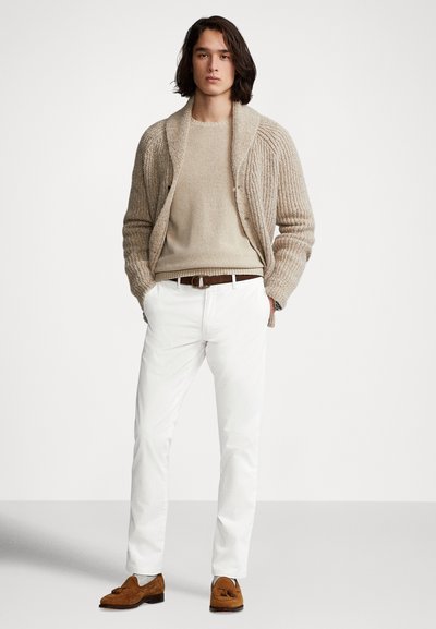 Beżowy sweter na guziki z dzianiny na jasnobeżowym swetrze, do tego białe spodnie i brązowe mokasyny. Sweter i kardigan o fakturze, swobodny krój.