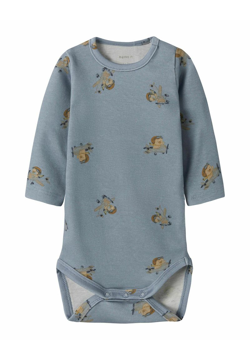 Bodystocking za bebe s dugim rukavima u mekom plavom pamuku, s malim ilustracijama pilota i aviona. Dugmadi za kopčanje na dnu za jednostavno oblačenje.