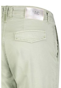 Ljusgröna bomullsshorts med silverfärgad "MAC"-etikett, bakficka, bältesöglor och en slät yta. Har en enkel design och rena linjer.