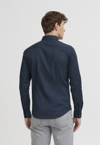 Tummansinisessä nappipaidassa on jämäkkä kaulus, pitkät hihat ja sileä pinta. Paidassa on slim fit -leikkaus ja huomaamaton selkäkaulusdesign.