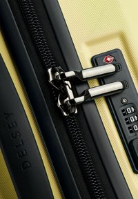 Valigia gialla con superficie testurizzata, una cerniera nera, cerniere in metallo argentato e una combinazione di lucchetto con un accento rosso.