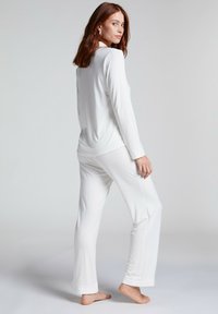 Witte pyjama-set van zacht materiaal, met lange mouwen en rechte pijpen met cuffs bij de enkels. Glad textuur zonder patronen.