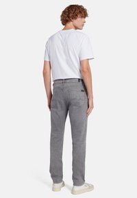 Jeans in denim grigioc con una vestibilità dritta, caratterizzati da due tasche posteriori e dettagli di cucitura sottili, abbinati a una t-shirt bianca semplice.