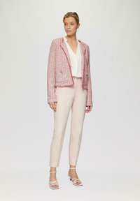 Rode en witte tweed blazer, cropped ontwerp met twee knopen, gecombineerd met lichtroze, op maat gemaakte broeken en witte sandalen met bandjes.
