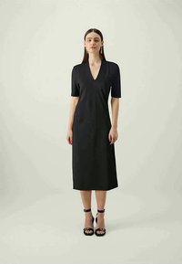 Czarna sukienka do kolan z dekoltem w serek, krótkimi rękawami i dopasowanym krojem. Gładki materiał, minimalistyczny design, zestawiona z czarnymi sandałami na obcasie.