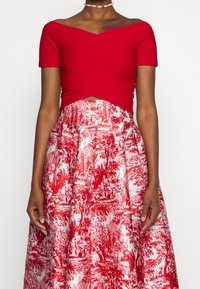 Červený vypasovaný crop top s krátkými rukávy, zkombinovaný s sukní po kolena s texturou, která má vzor bílé a červené toile.