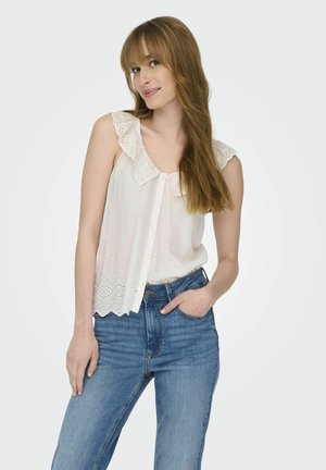 Blusa blanca con detalles de ojal, hombros con volantes y cierre de botones, combinada con jeans de tiro alto azules. Textura suave.