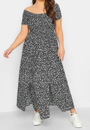 Czarna maxi sukienka w kwiaty z opuszczanymi ramionami, marszczonym gorsetem i białymi kwiatowymi wzorami, połączona z białymi trampkami.