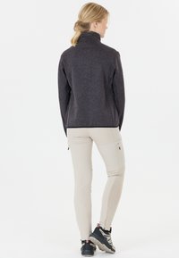 Grå fleecejacka med hög krage, avsmalnande passform och flatlocksömmar, kombinerad med beige stretchiga byxor och svarta vandringsskor.