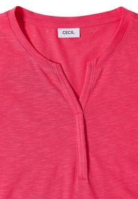Top en maille rose vif avec un col rond et une fente à l’avant, avec une étiquette "CECIL" cousue à l’intérieur du col.
