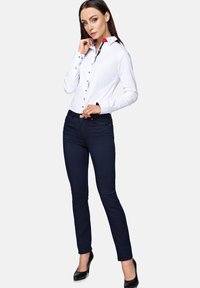 White fitted shirt with a red and navy collar detail, paired with navy skinny jeans and black heels. Smooth fabric with button accents.